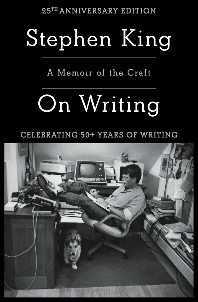 A black and white photograph of a man sitting in a chair with his feet on a desk, surrounded by books, a computer, and other writing tools, with a dog sitting beside him.